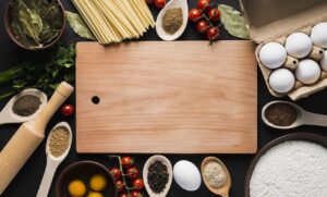 まな板のまわりにパスタ・卵・トマト・香辛料などの食材が並んだ写真